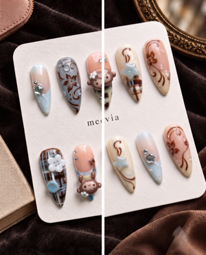 Brown plaid press-on nails with monkey charms, floral details, blue buttons, and rhinestone accents