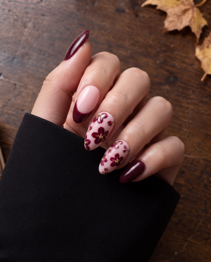Burgundy floral French tip press-on nails with gold bead accents on a soft pink base
