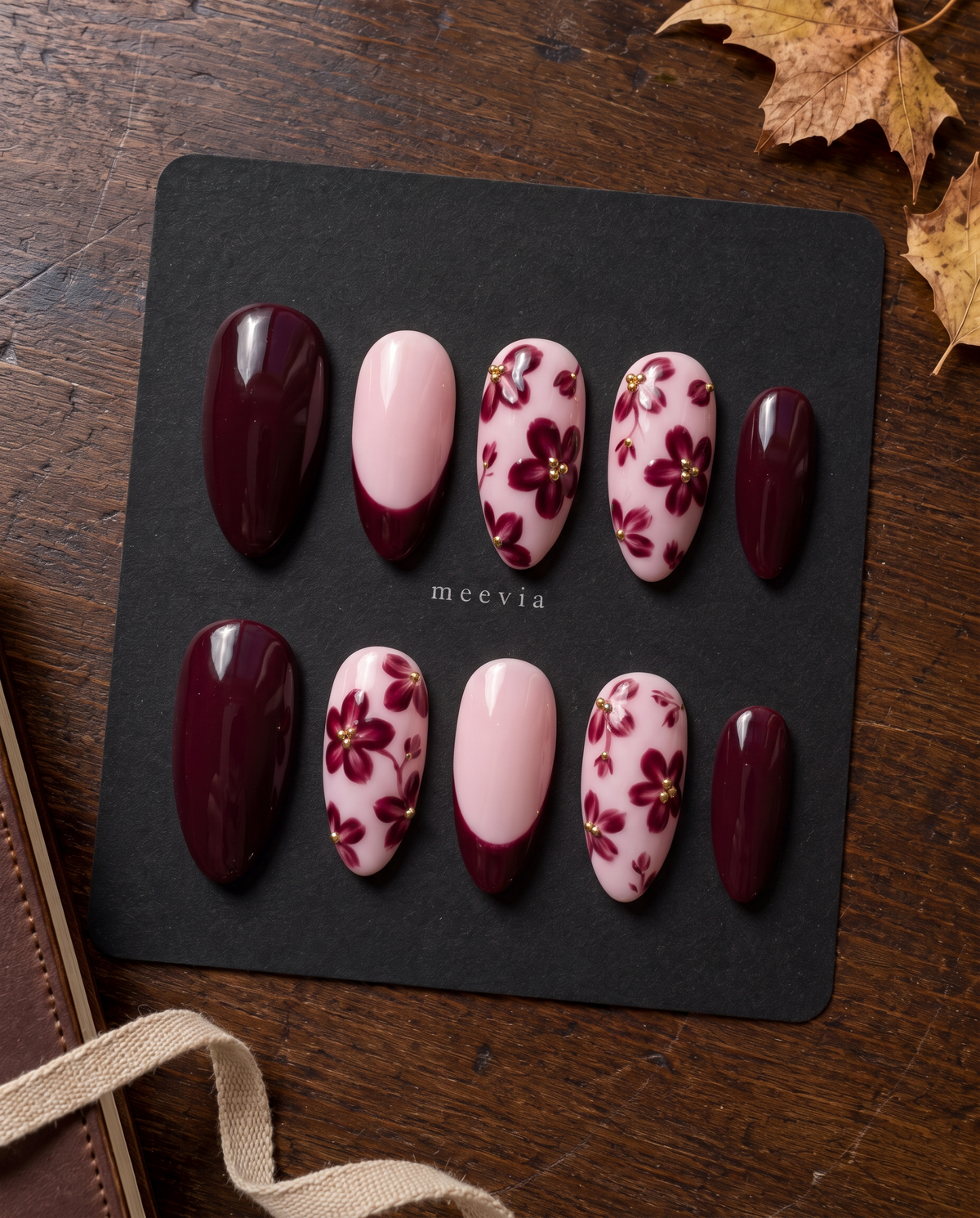 Burgundy floral French tip press-on nails with gold bead accents on a soft pink base