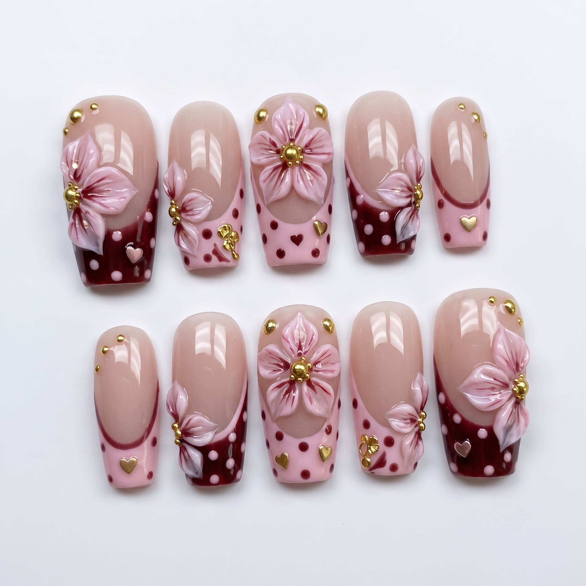 Burgundy French tip press-on nails with 3D pink flowers, gold studs, and polka dot patterns.