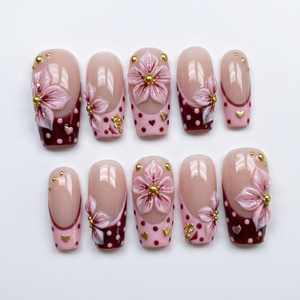Burgundy French tip press-on nails with 3D pink flowers, gold studs, and polka dot patterns.