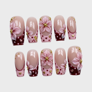 Burgundy French tip press-on nails with 3D pink flowers, gold studs, and polka dot patterns.