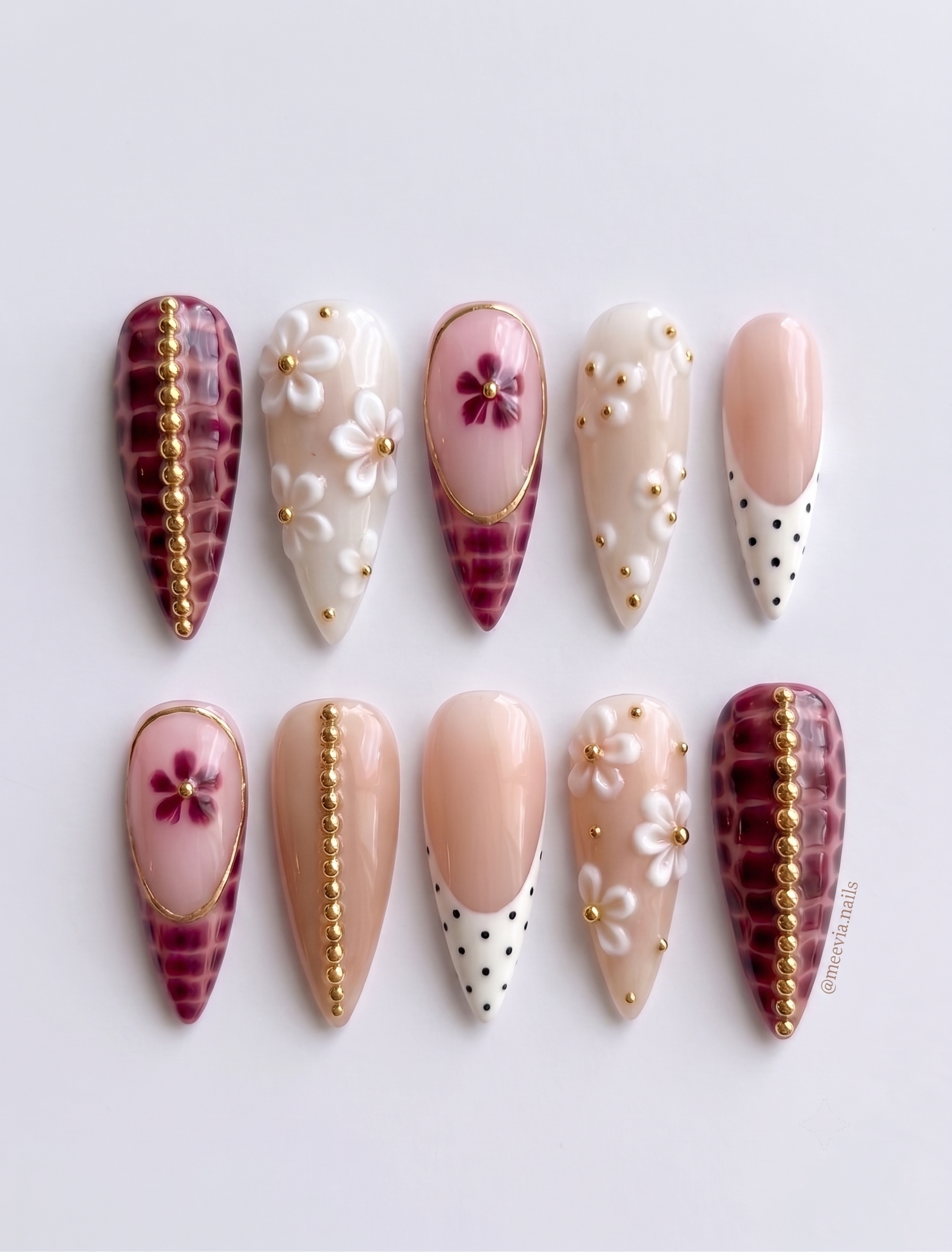 A set of stiletto press-on nails featuring burgundy croc print, white floral accents, gold bead details, and polka dot French tips.