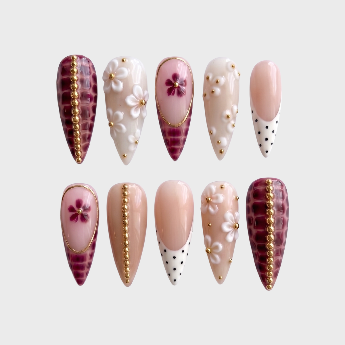 A set of stiletto press-on nails featuring burgundy croc print, white floral accents, gold bead details, and polka dot French tips.