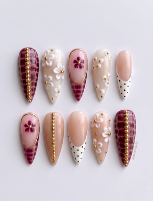 A set of stiletto press-on nails featuring burgundy croc print, white floral accents, gold bead details, and polka dot French tips.