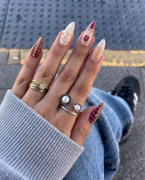 A set of stiletto press-on nails featuring burgundy croc print, white floral accents, gold bead details, and polka dot French tips.