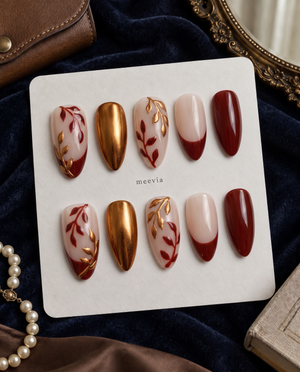 Burgundy and gold leaf floral press-on nails with nude bases and a burgundy French tip
