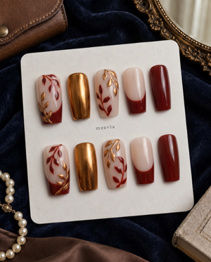 Burgundy and gold leaf floral press-on nails with nude bases and a burgundy French tip