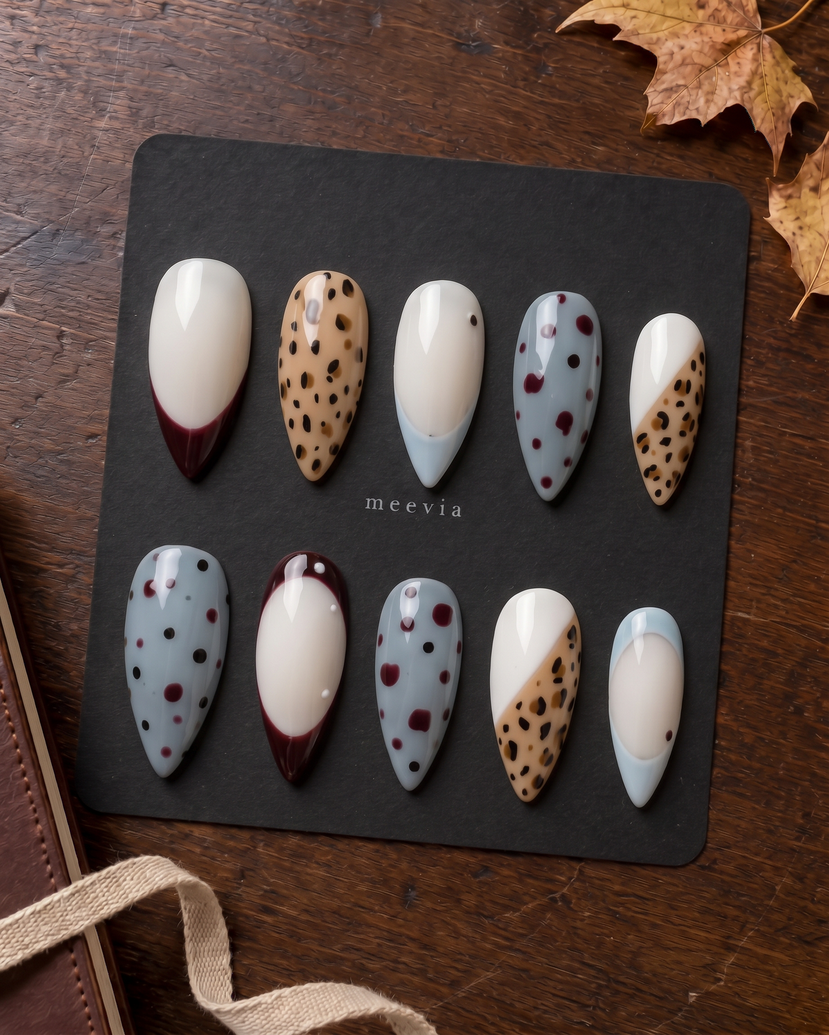 Glossy press-on nails with burgundy French tips, tan leopard print, creamy white bases, and blue dotted accents