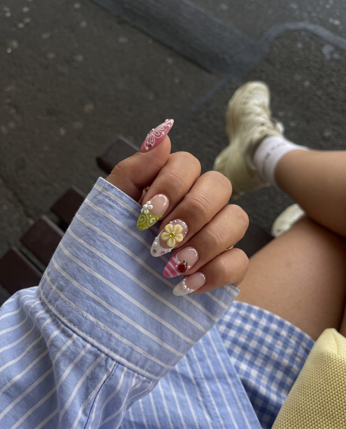 A set of glossy press-on nails decorated with 3D pink and yellow flowers, red ladybugs, white butterflies, and pearls on pink and green backgrounds.