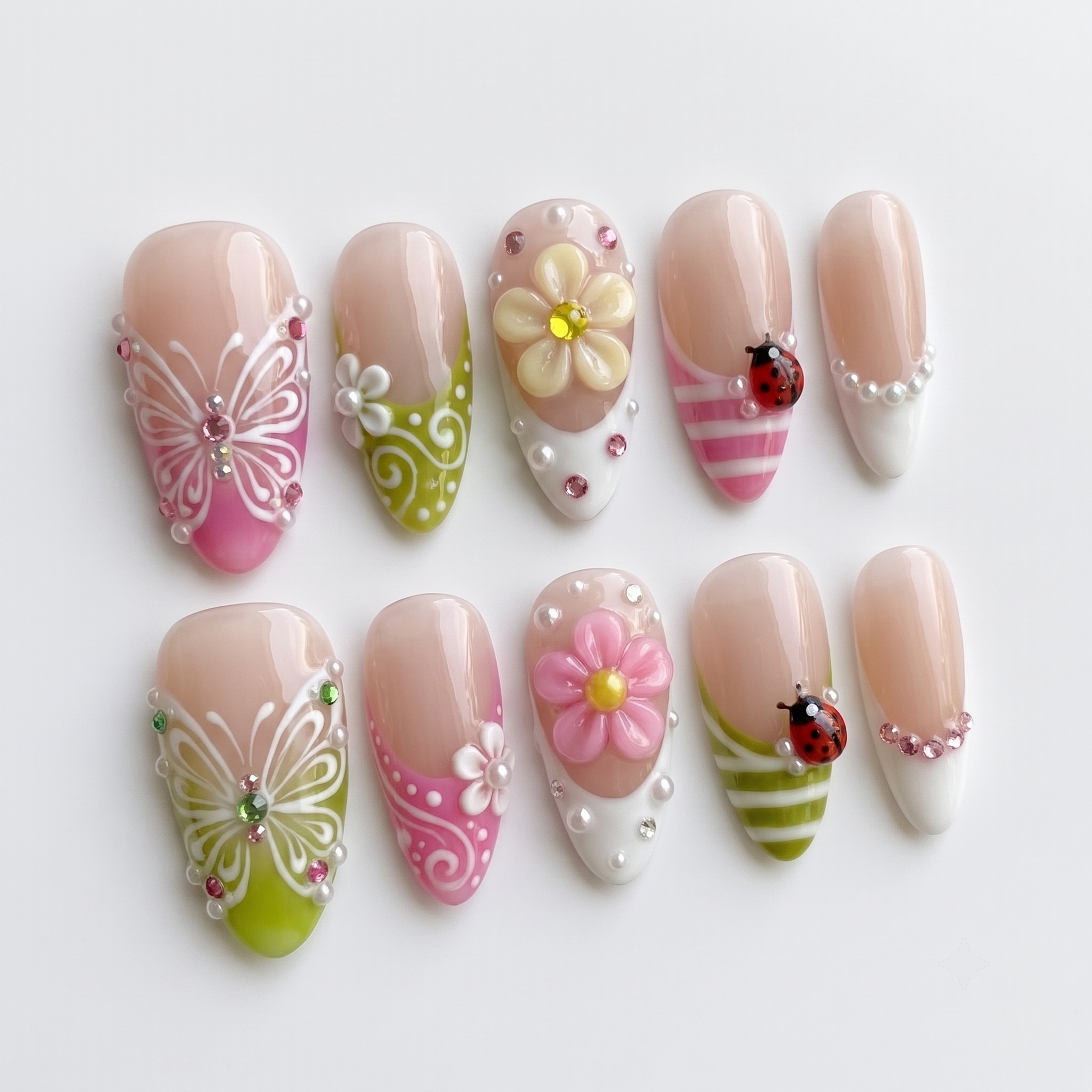 A set of glossy press-on nails decorated with 3D pink and yellow flowers, red ladybugs, white butterflies, and pearls on pink and green backgrounds.
