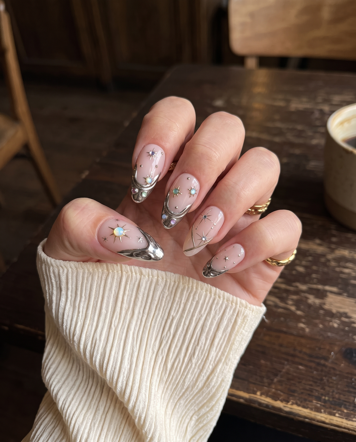 A set of pink press-on nails featuring gold metallic tips, celestial starburst details, and colorful iridescent gems.