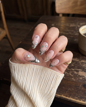 A set of pink press-on nails featuring gold metallic tips, celestial starburst details, and colorful iridescent gems.