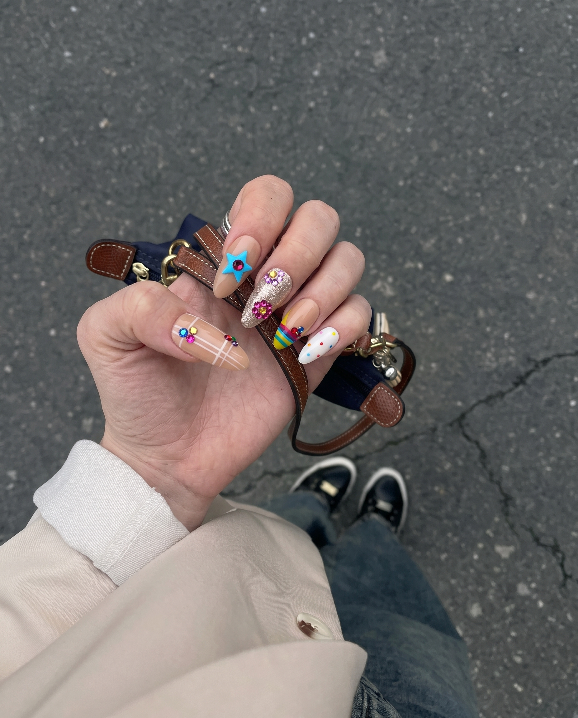 A set of press-on nails featuring nude bases with grid patterns, rainbow tips, glitter, and colorful 3D star and flower charms.