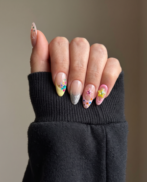 A set of pastel press-on nails featuring colorful star charms, rhinestone accents, and glitter French tips.