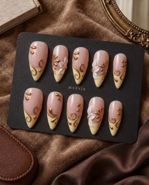 Glossy nude and cream press-on nails with white floral accents and raised gold swirls