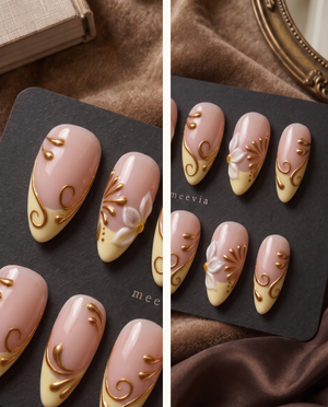 Glossy nude and cream press-on nails with white floral accents and raised gold swirls