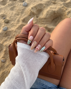 A set of eclectic press-on nails in pink, gold, and green featuring a 3D flower, face illustration, and rhinestone details.
