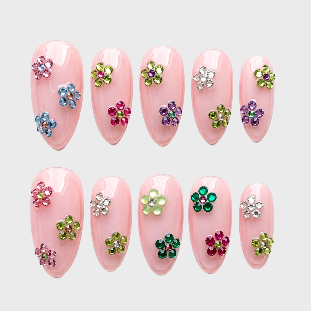 Blush pink press-on nails decorated with multi-colored rhinestone flower motifs.