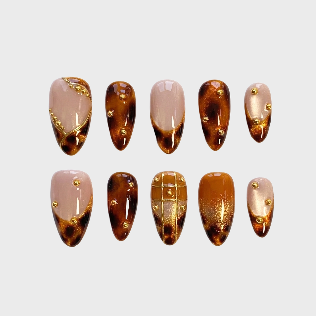 A set of tortoiseshell press-on nails featuring gold beads and gold leaf accents.