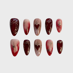 A set of press-on nails featuring deep red and nude tones, gold star motifs, and heart designs.