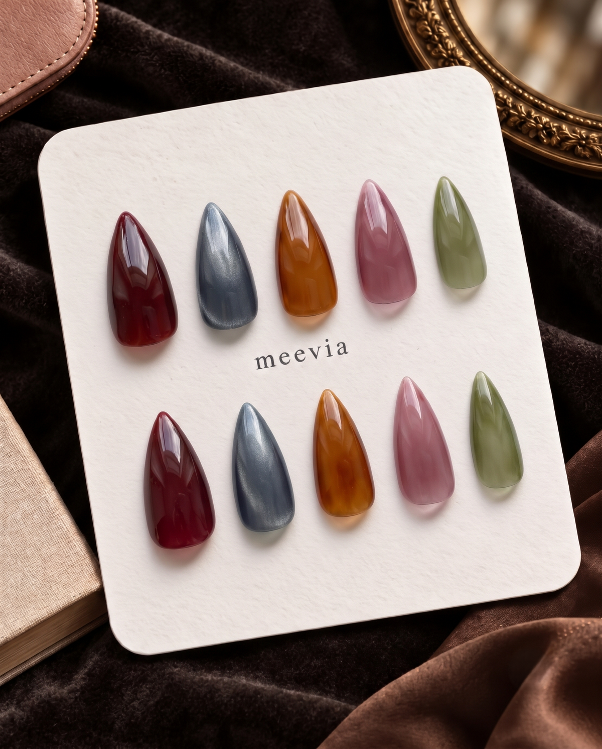 Glossy almond press-on nails in translucent burgundy, slate blue, amber, mauve, and olive green tones