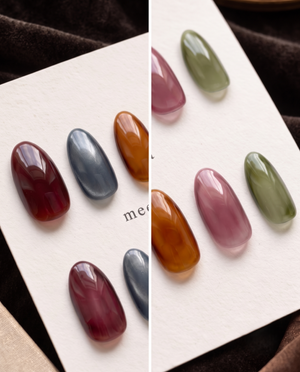 Glossy almond press-on nails in translucent burgundy, slate blue, amber, mauve, and olive green tones