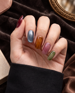 Glossy almond press-on nails in translucent burgundy, slate blue, amber, mauve, and olive green tones
