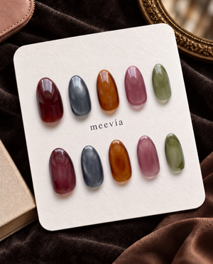Glossy almond press-on nails in translucent burgundy, slate blue, amber, mauve, and olive green tones
