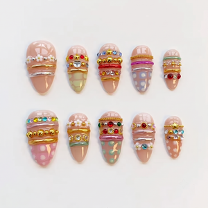 A set of ten nude press-on nails decorated with colorful rhinestones, gold chains, silver bands, white flower charms, and pastel patterns.