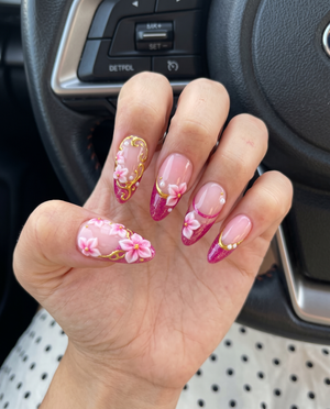 A set of magenta glitter French tip press-on nails decorated with 3D floral designs, gold filigree, and small white pearls.
