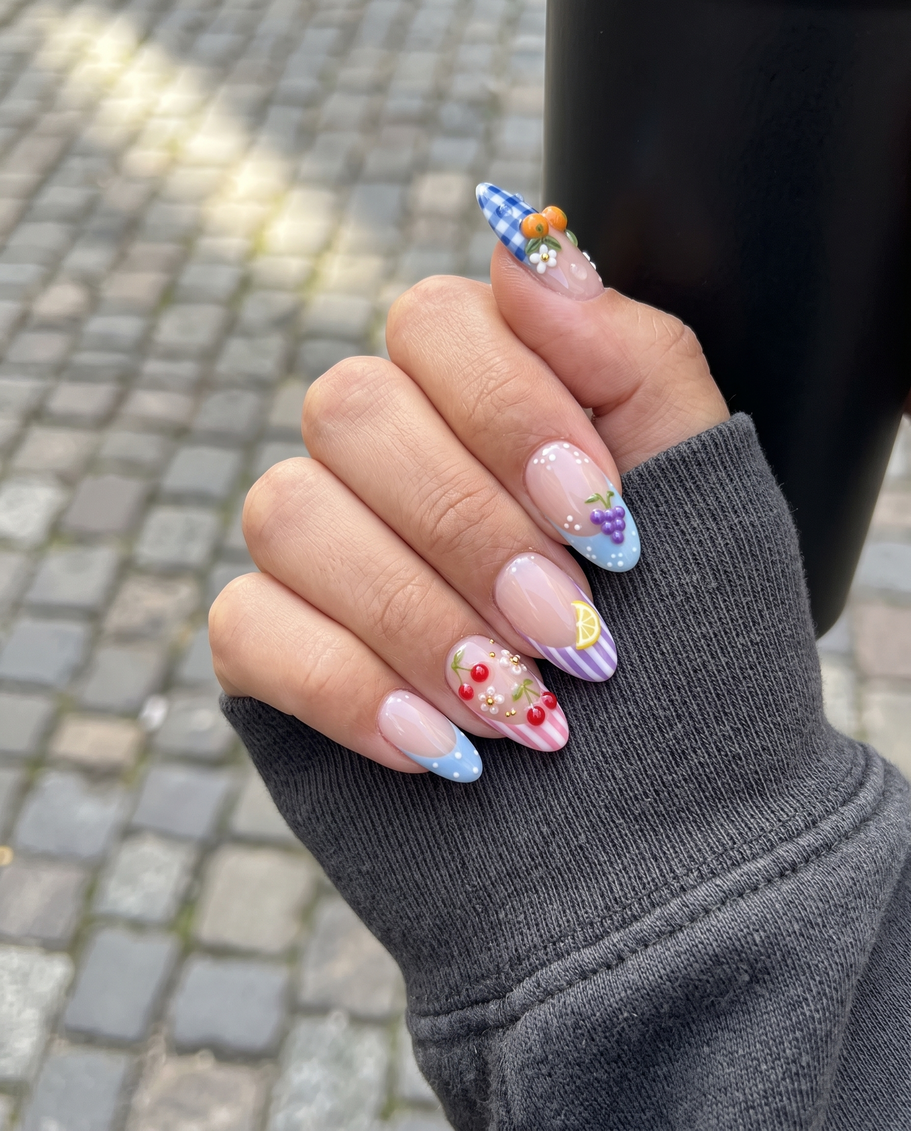 A set of press-on nails featuring gingham patterns, fruit motifs like oranges and cherries, and French tips on a white background.