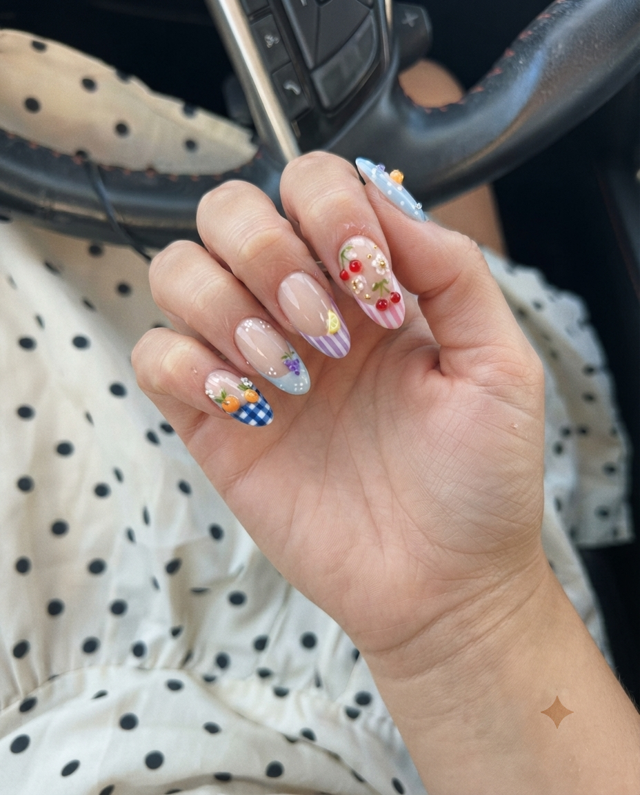 A set of press-on nails featuring gingham patterns, fruit motifs like oranges and cherries, and French tips on a white background.