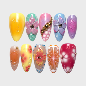 A collection of colorful press-on nails featuring 3D floral designs, water droplets, and gold bead embellishments.