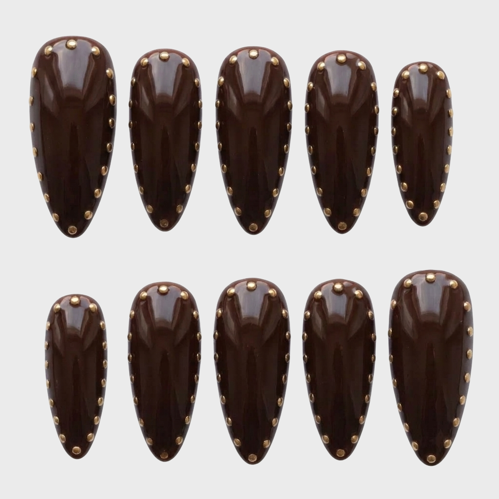 Set of glossy chocolate brown stiletto press-on nails decorated with gold studs along the edges.