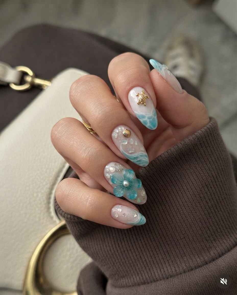 A set of sheer pink press-on nails featuring turquoise ocean wave designs, gold sea turtle and starfish charms, and 3D blue flowers with pearl details.