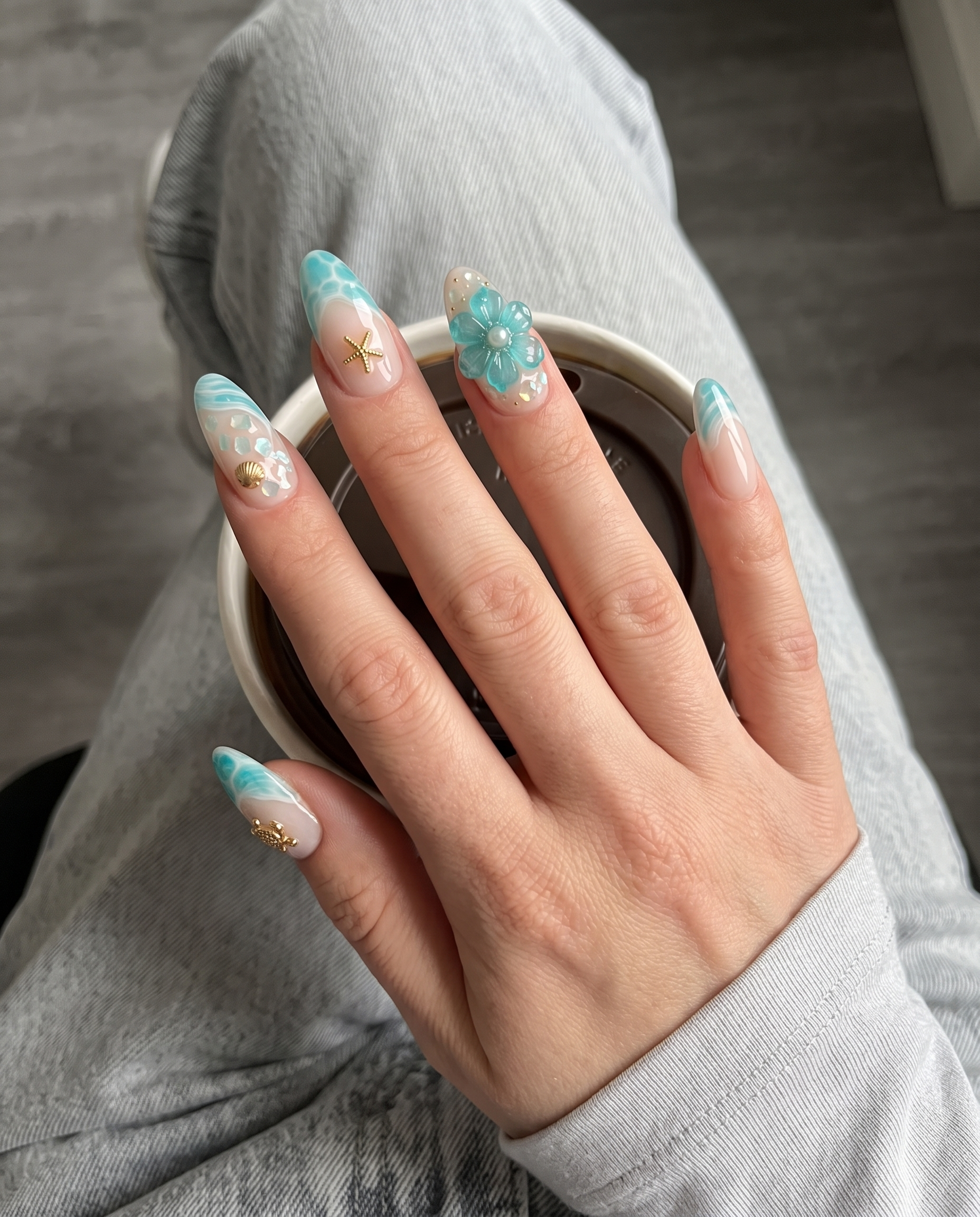 A set of sheer pink press-on nails featuring turquoise ocean wave designs, gold sea turtle and starfish charms, and 3D blue flowers with pearl details.