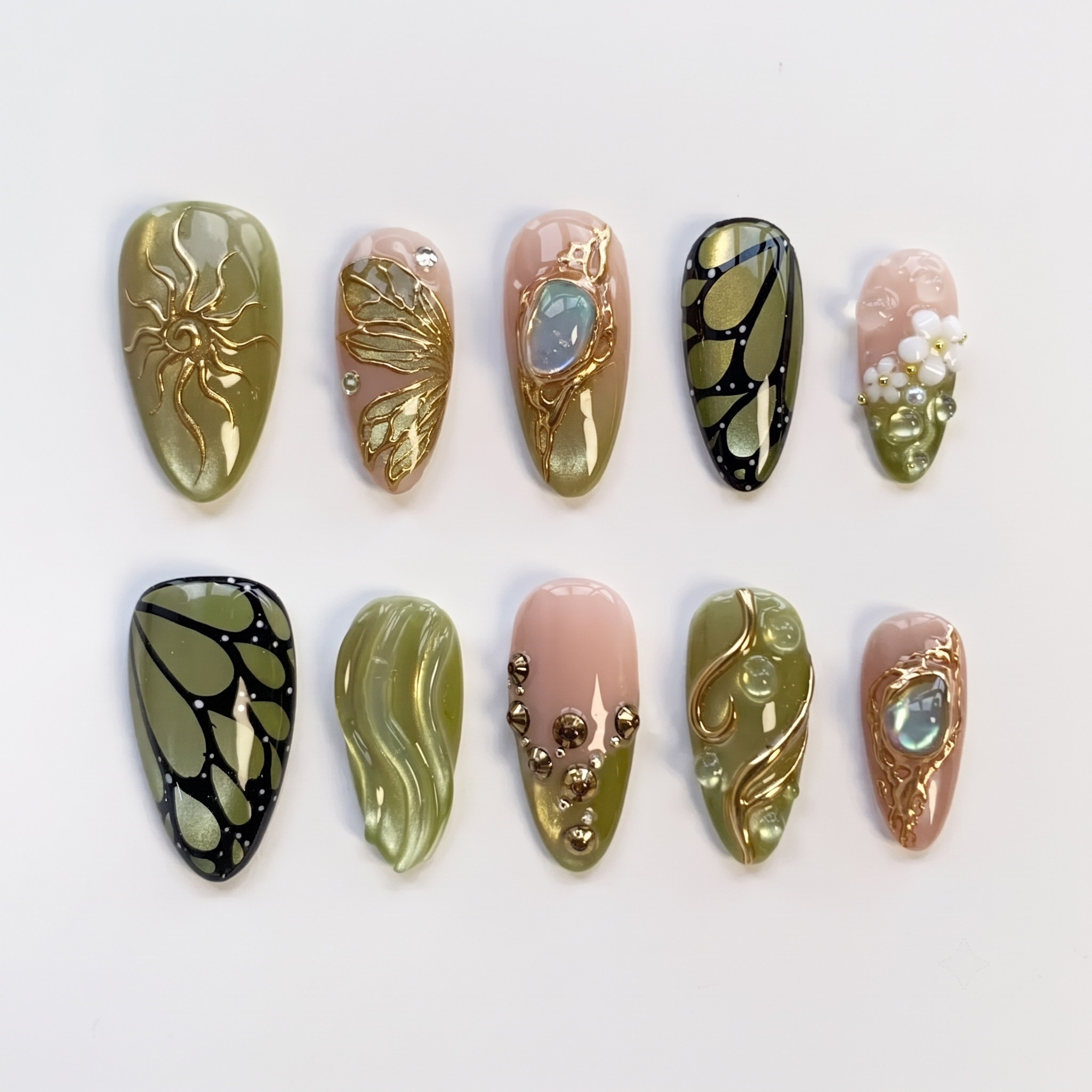 A set of press-on nails featuring olive green and pink bases decorated with gold butterfly wings, 3D flowers, and a large gemstone.