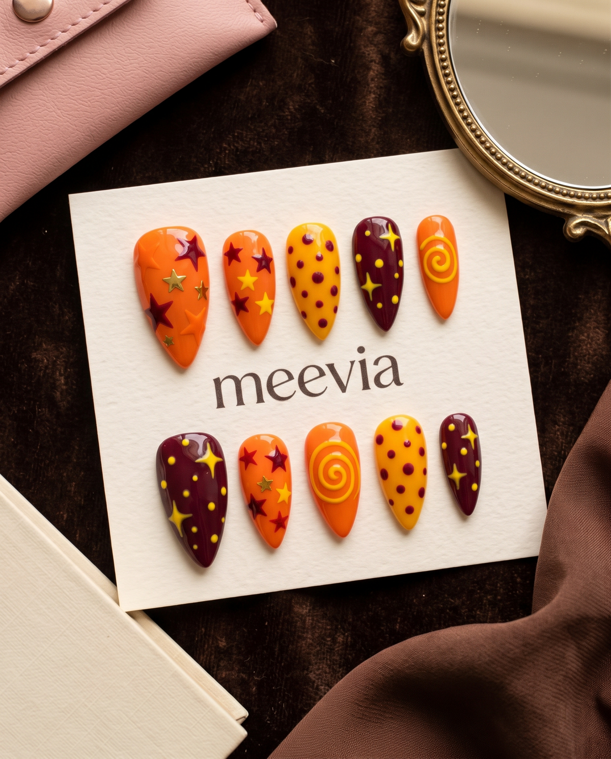 Orange and maroon celestial press-on nails with stars, dots, and swirl designs