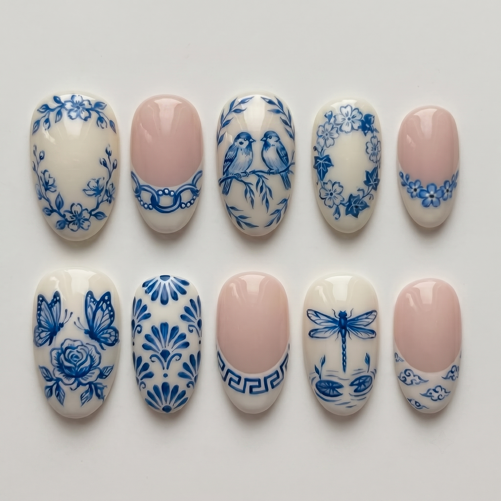 Glossy blue and white press-on nails featuring detailed porcelain-style illustrations of birds, butterflies, dragonflies, and flowers.