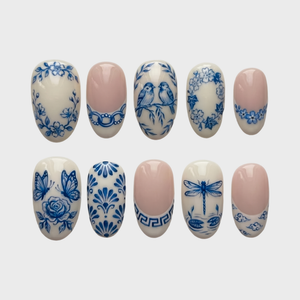 Glossy blue and white press-on nails featuring detailed porcelain-style illustrations of birds, butterflies, dragonflies, and flowers.