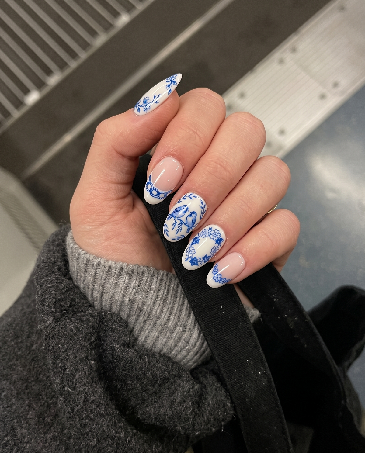 Glossy blue and white press-on nails featuring detailed porcelain-style illustrations of birds, butterflies, dragonflies, and flowers.