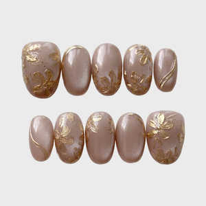 A set of oval press-on nails featuring a dusty pink shimmer base decorated with 3D metallic gold flowers and gold line accents.