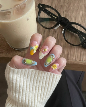 3D pastel press-on nails featuring yellow flowers, white seashells, gold accents, and a pink and blue gradient background.
