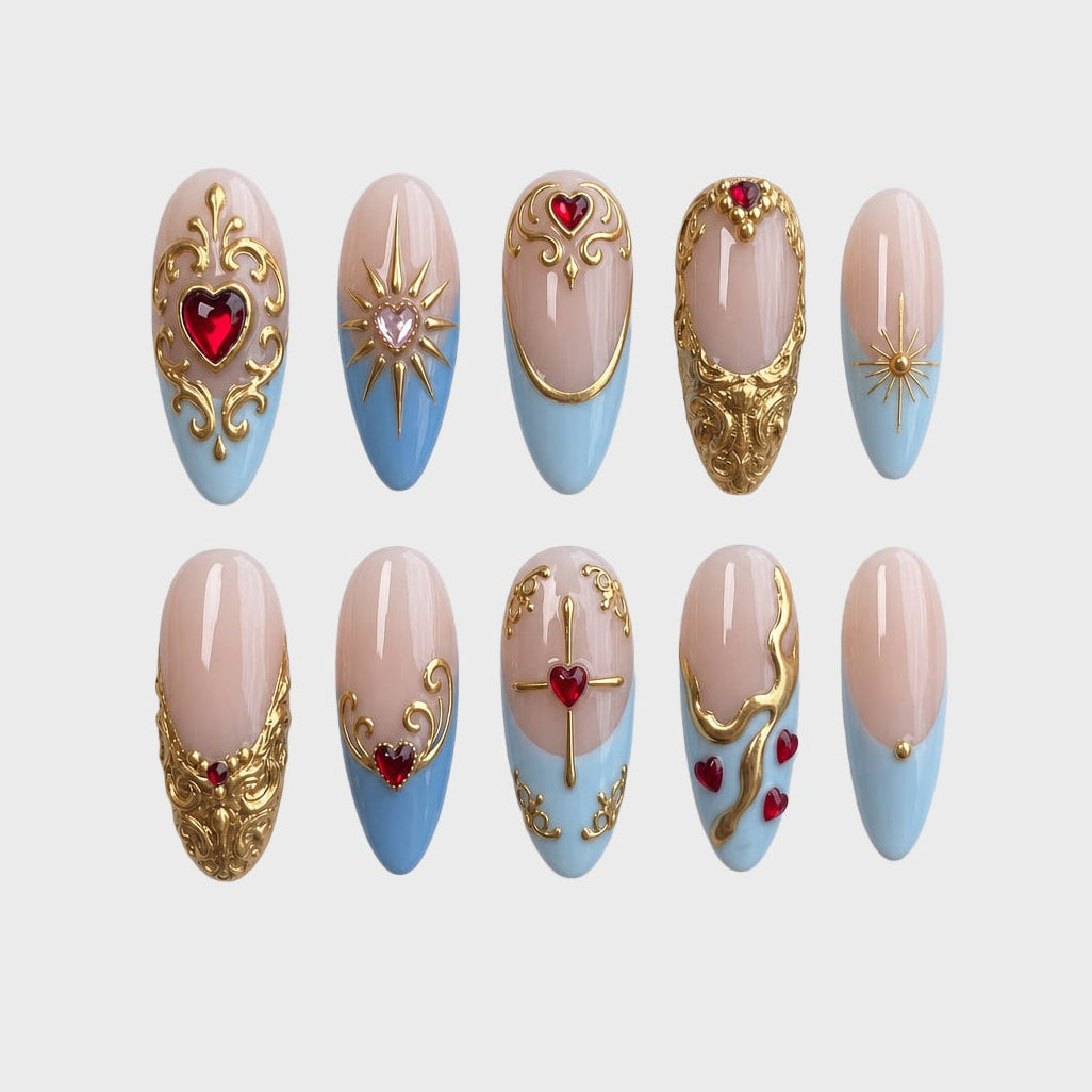 A set of press-on nails featuring light blue French tips, ornate gold baroque filigree, and red heart gems.