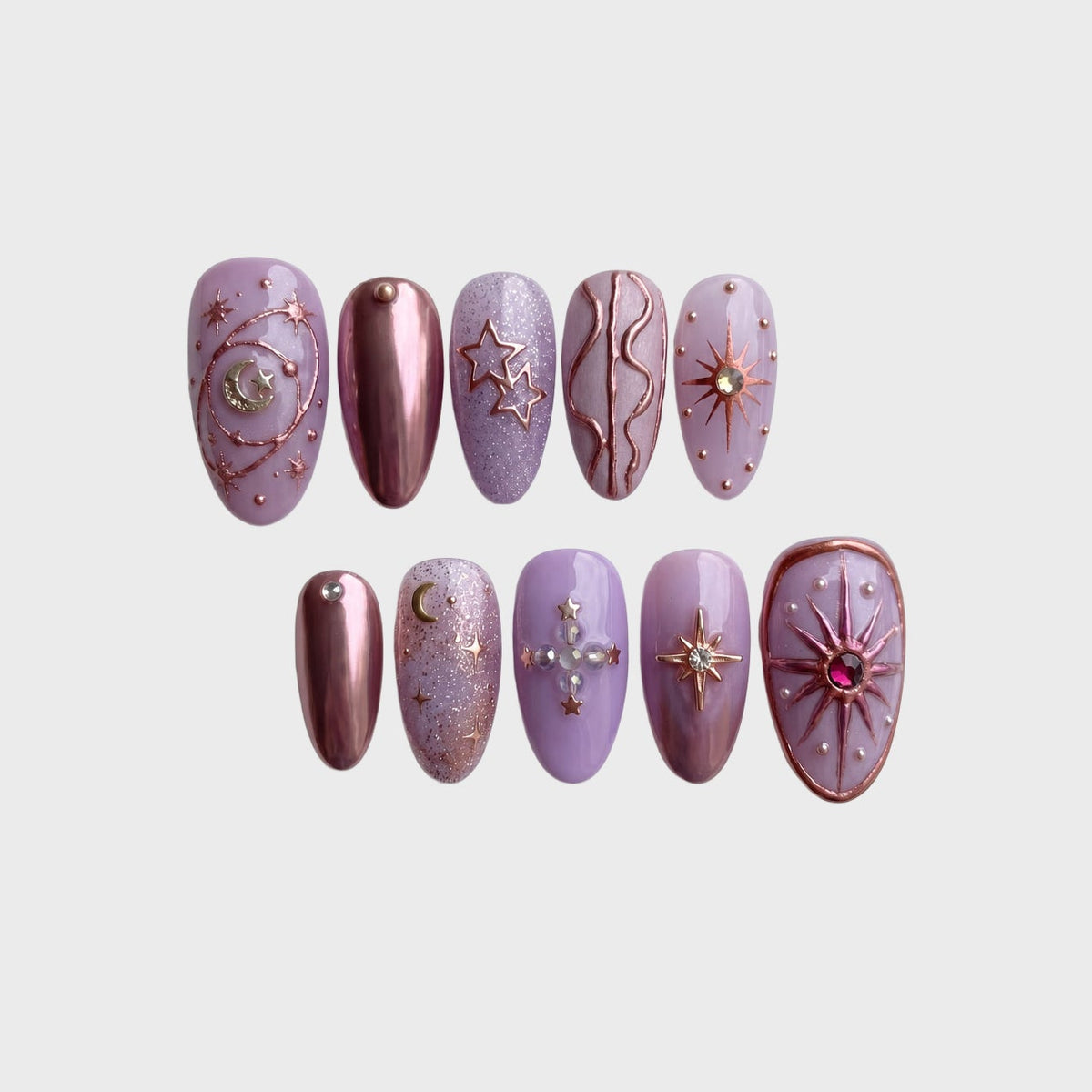 Lavender press-on nails decorated with metallic rose gold celestial designs, stars, moons, and rhinestones.