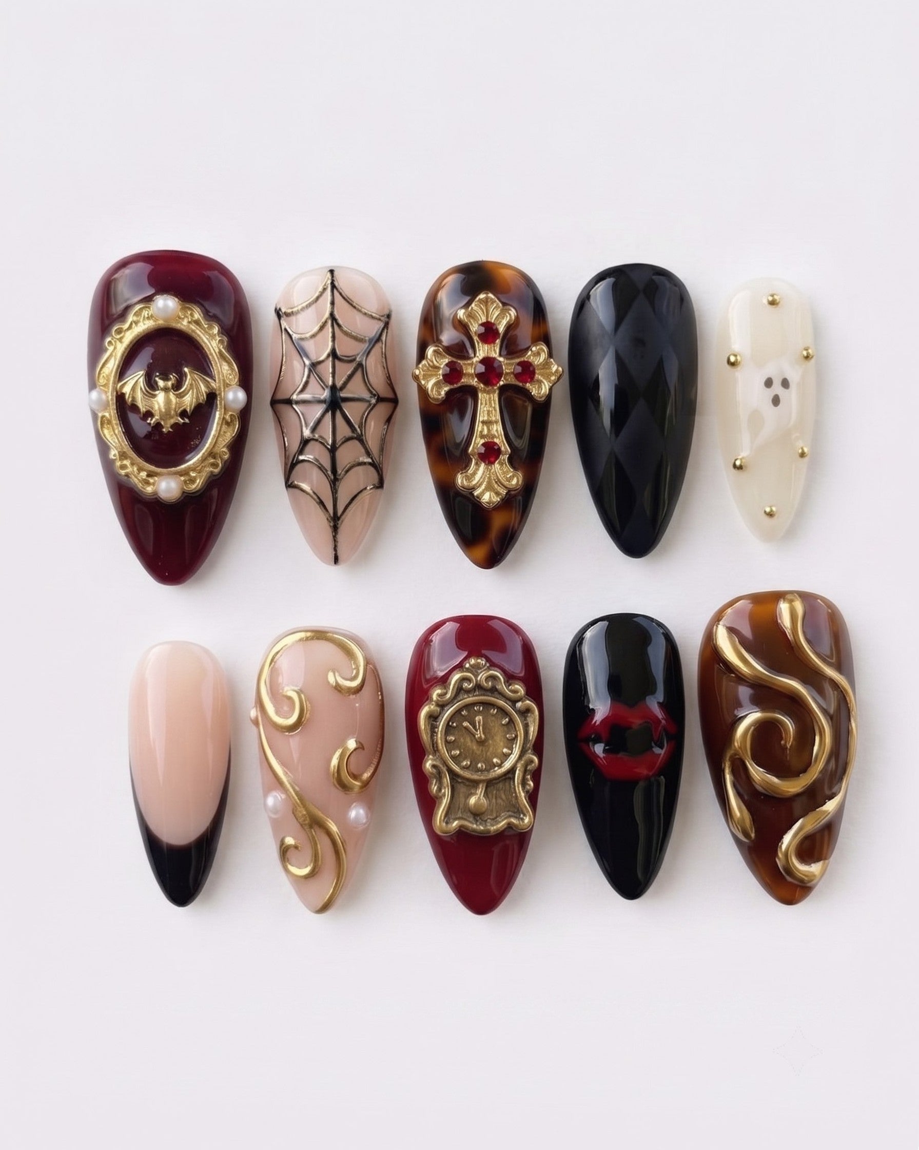 Gothic press-on nails featuring gold baroque embellishments, a bat, a cross, spiderwebs, and vampire lips on burgundy and black bases.