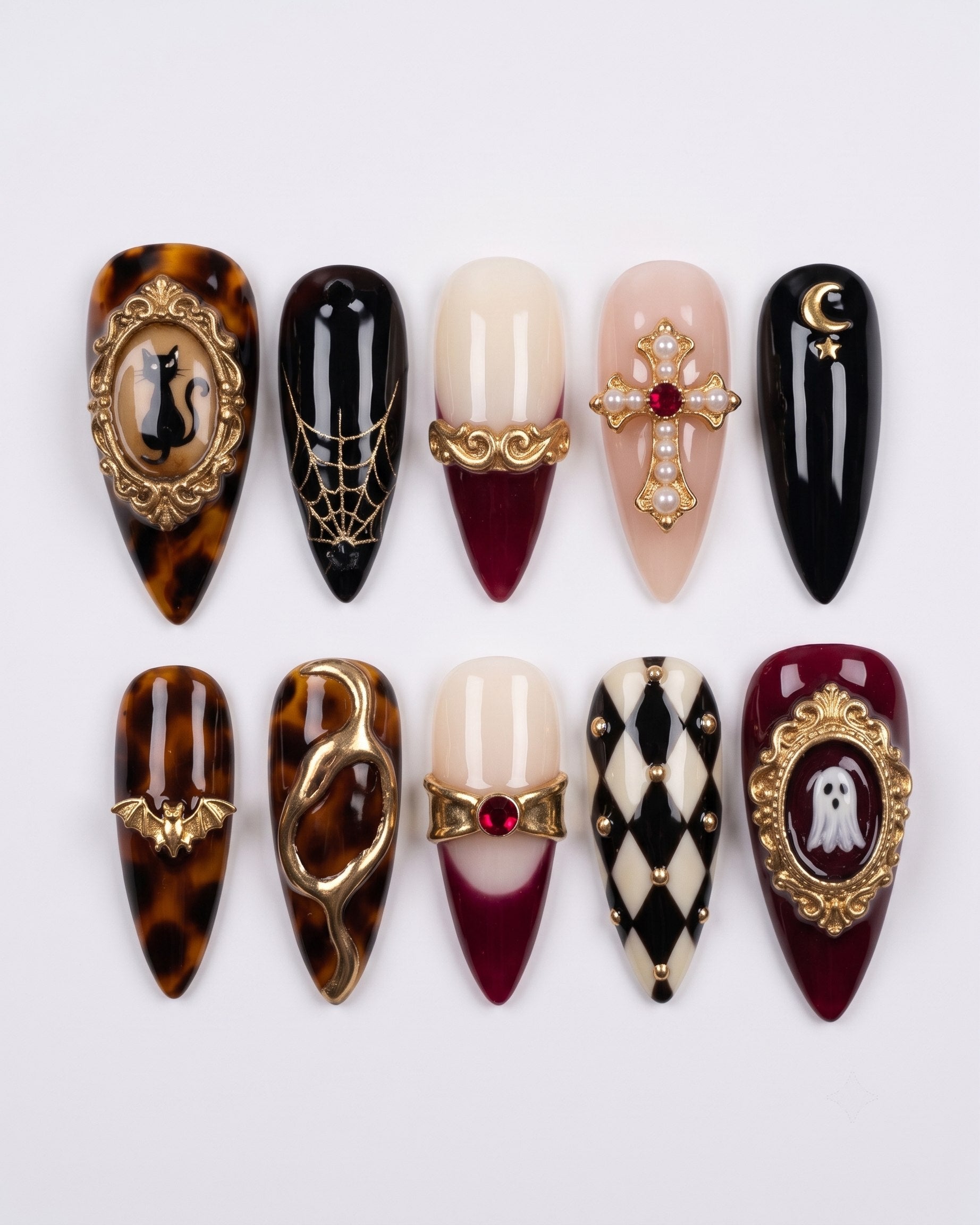 A set of gothic themed press-on nails featuring gold charms, cat and ghost motifs, tortoise shell patterns, and a harlequin design.