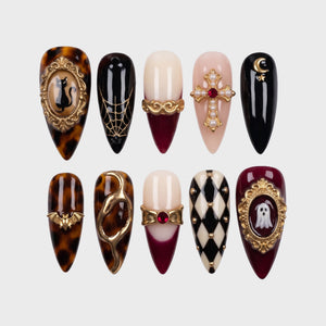 A set of gothic themed press-on nails featuring gold charms, cat and ghost motifs, tortoise shell patterns, and a harlequin design.