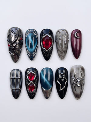 A set of gothic press-on nails featuring black, grey marble, and teal cat-eye bases with silver metallic spider, ghost, crescent moon, and red gemstone details.